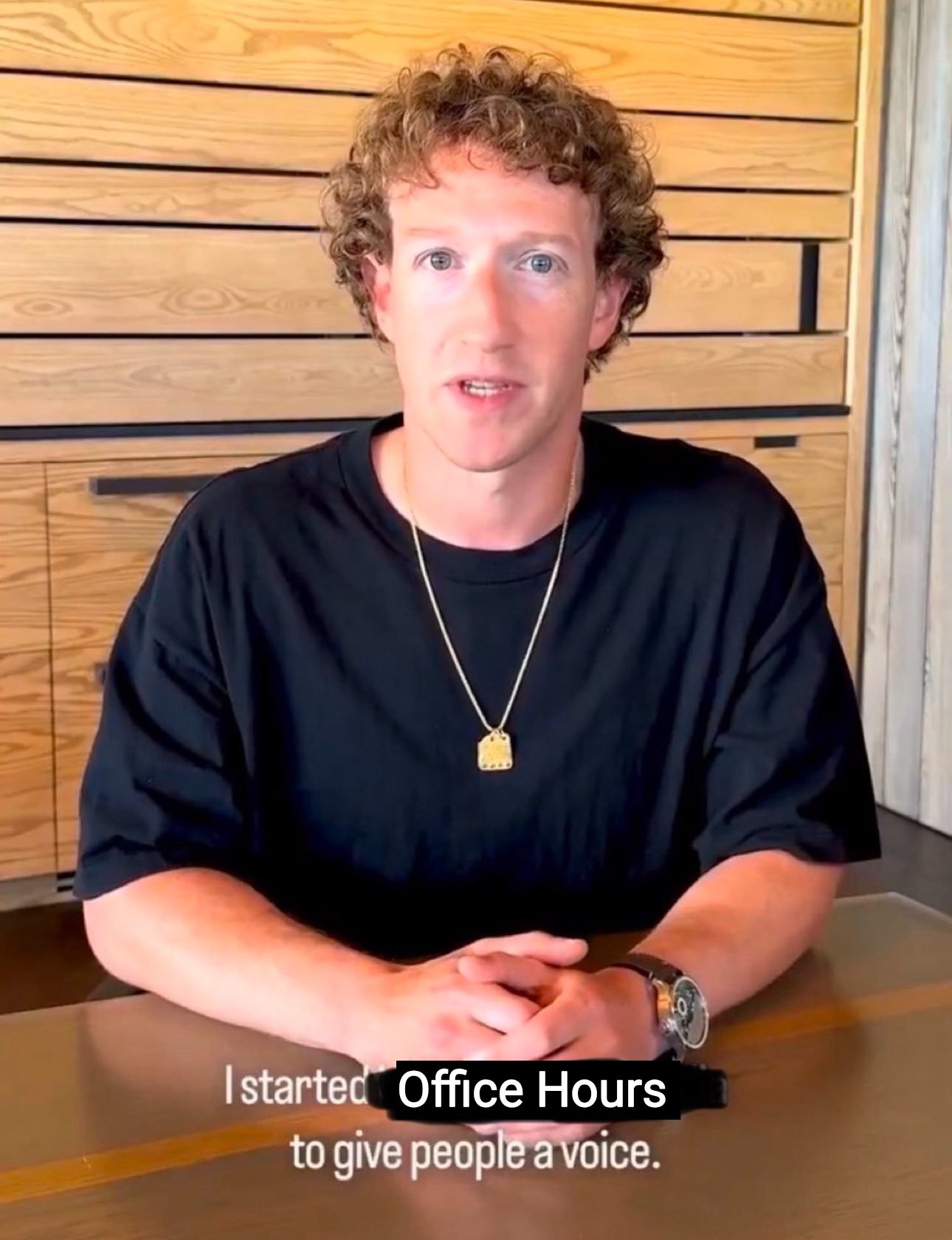 A man with curly hair wearing a black t-shirt and a gold chain necklace sits at a table with his hands clasped. Text at the bottom of the image reads, "I started Office Hours to give people a voice."