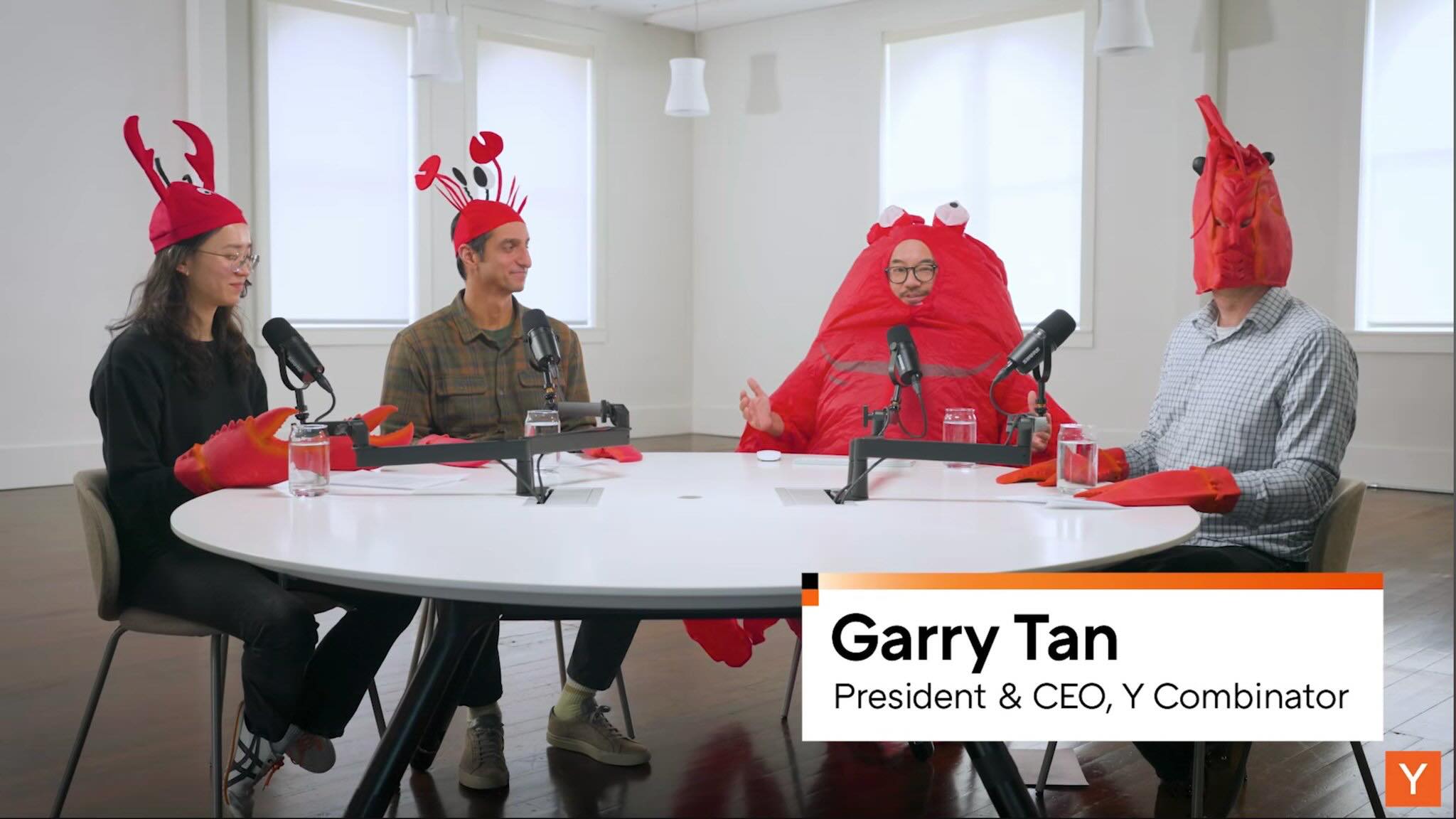 Four people dressed in red lobster costumes sit around a white table with microphones, engaged in a podcast-style discussion; one person is identified as Garry Tan, President & CEO of Y Combinator.