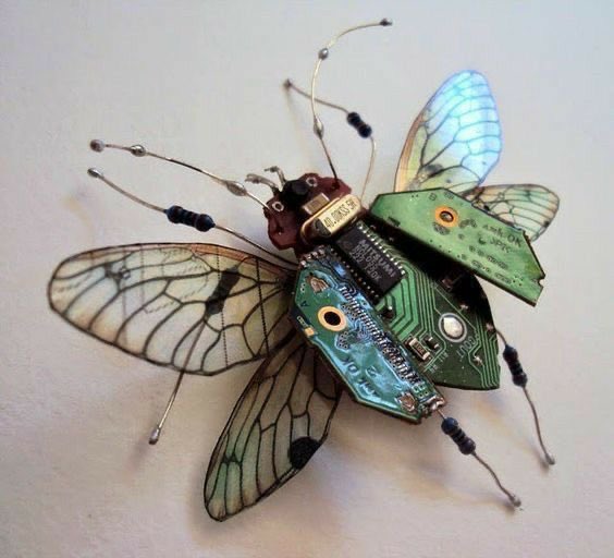 A close-up, high-angle shot shows a mechanical insect made from circuit boards and wires. The insect has four translucent wings with black veins, a dark brown head, and a body made of green circuit boards with various electronic components.